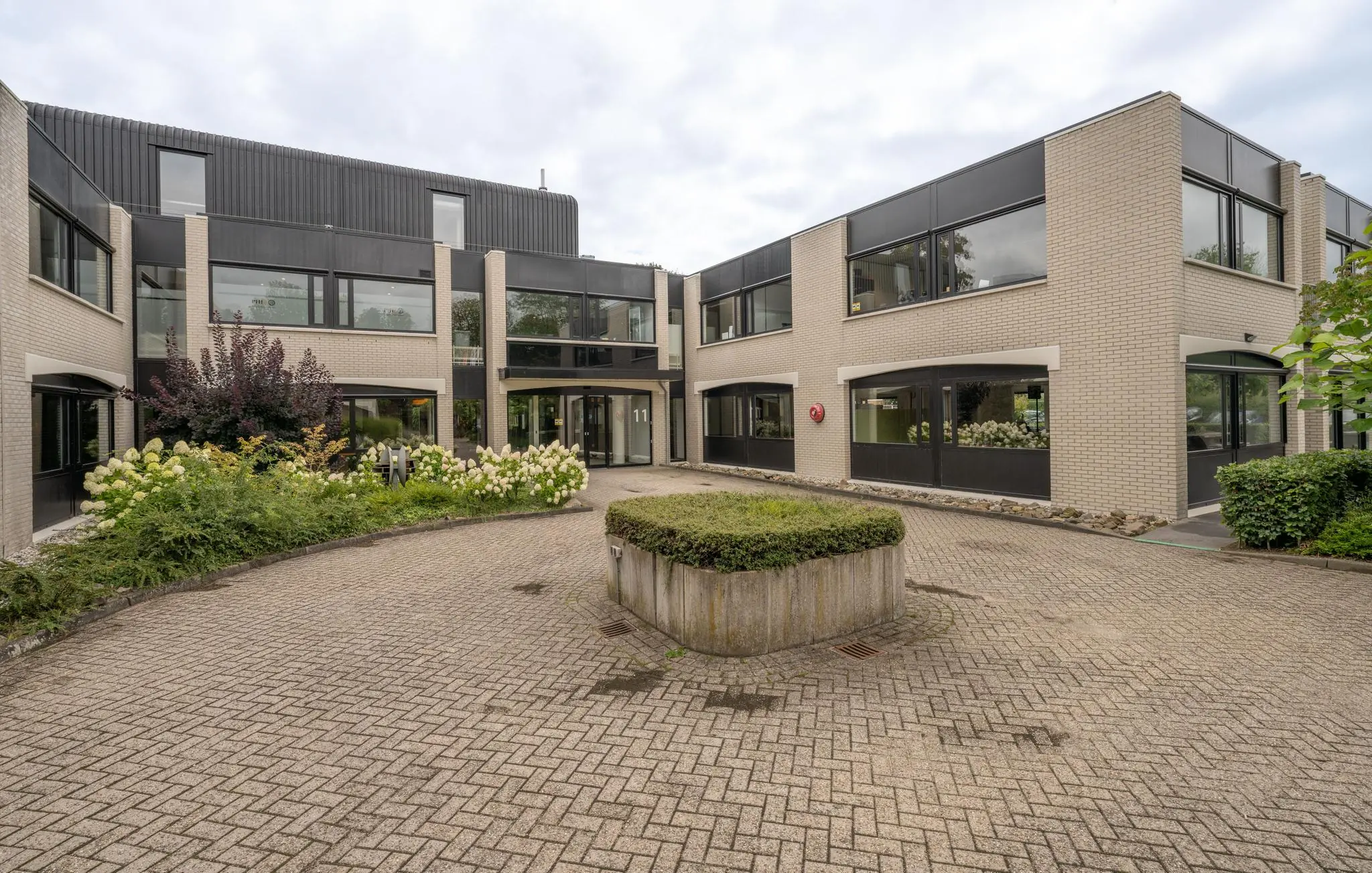 Moderne kantoor- of zorginstelling aan de Burgemeester Verderlaan met een betegelde binnenplaats en bloeiende beplanting.